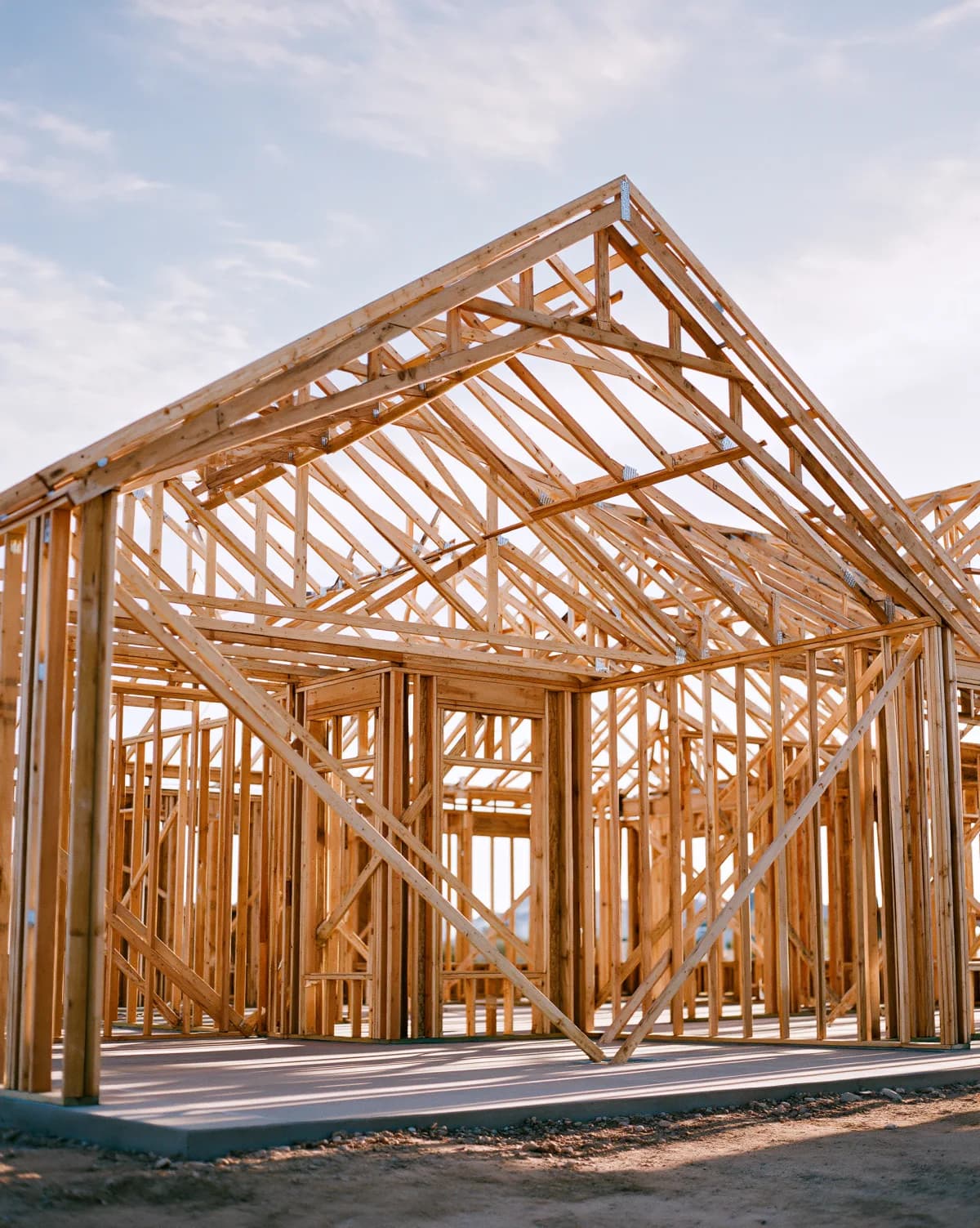 A house mid-construction, exposed wood framing and roof trusses standing on the slab